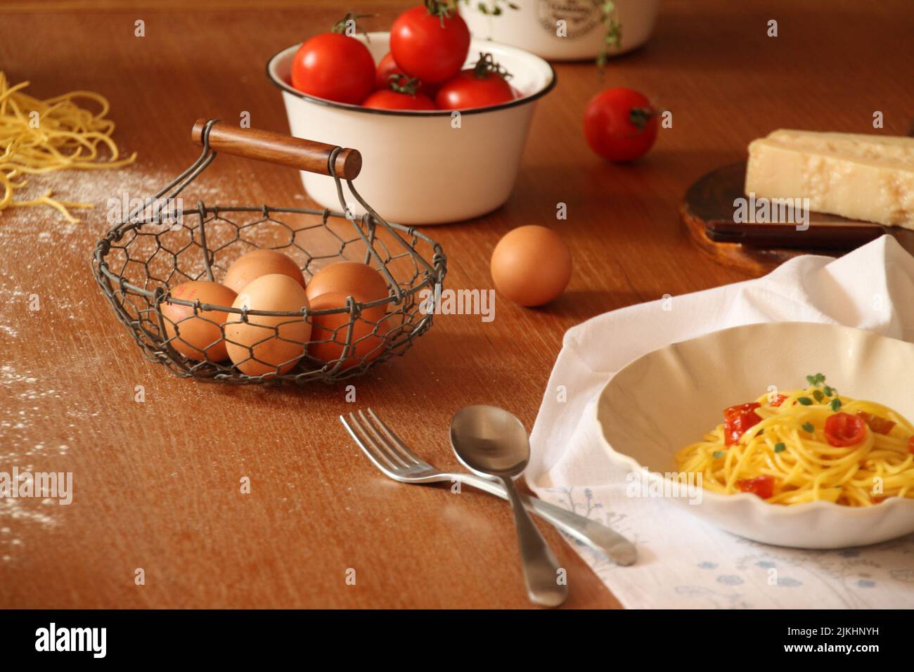 Stillleben eines hölzernen Küchentischs mit rohen Eiern und Tomaten, Käse und gekochter Pasta Stockfoto