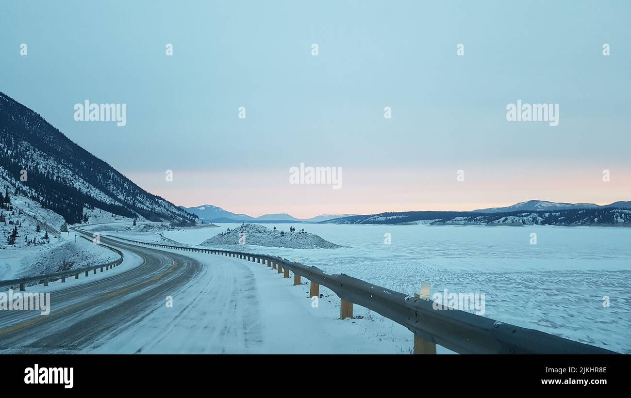 Eine perspektivische Aufnahme einer Autobahn neben einem Feld und einem Berg im Winter. Stockfoto