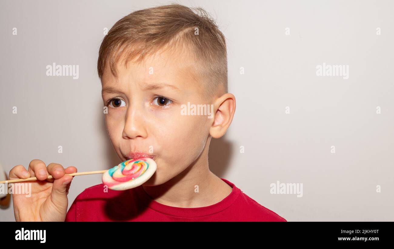 Portrait eines glücklichen Jungen, der süße Bonbons leckt. Nahaufnahme auf weißem Hintergrund Stockfoto