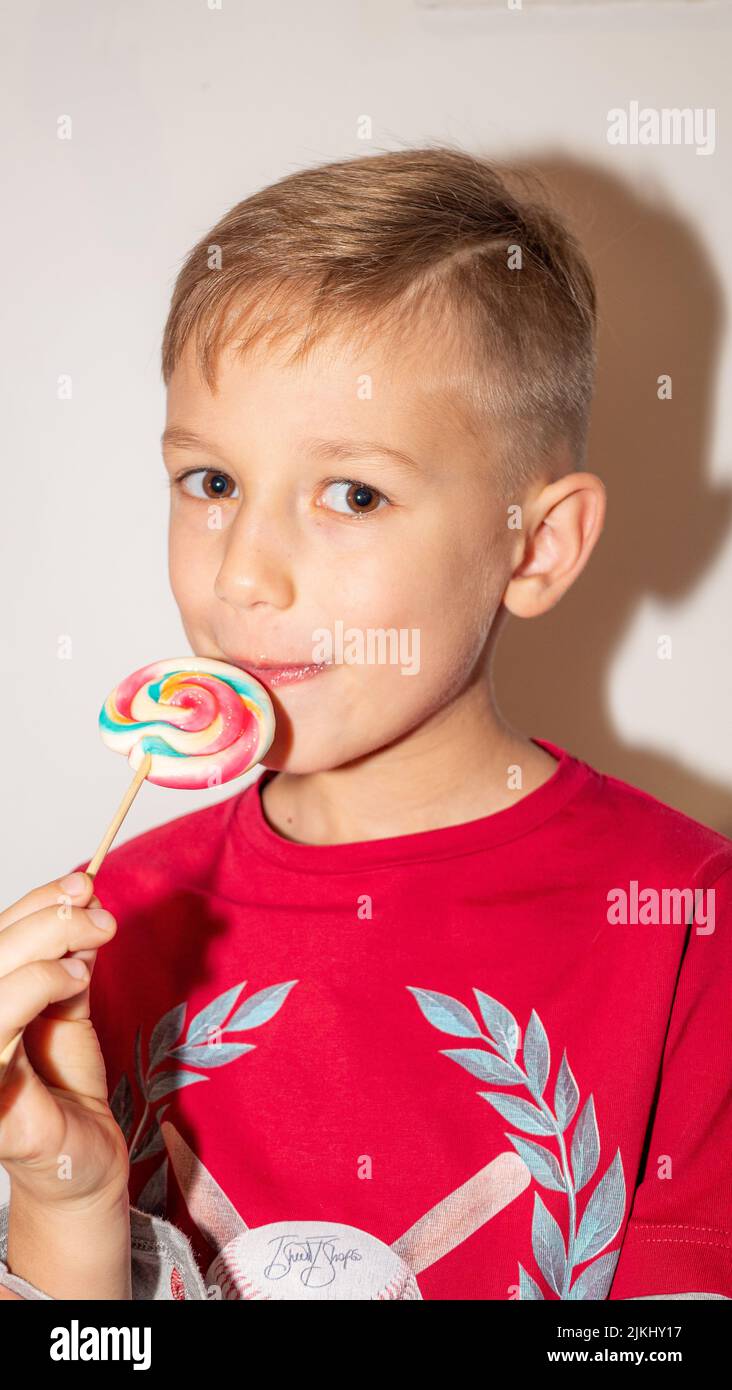Portrait eines glücklichen Jungen, der süße Bonbons leckt. Nahaufnahme auf weißem Hintergrund Stockfoto