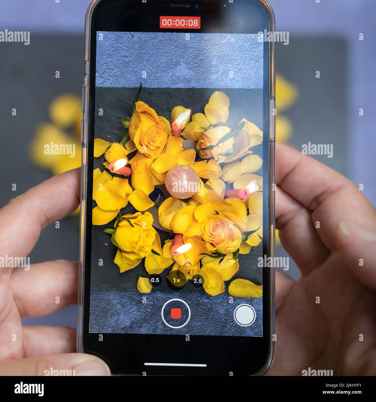 Eine Nahaufnahme eines Telefons, das ein Video von Rosenblättern und Kerzen aufzeichnet. Stockfoto