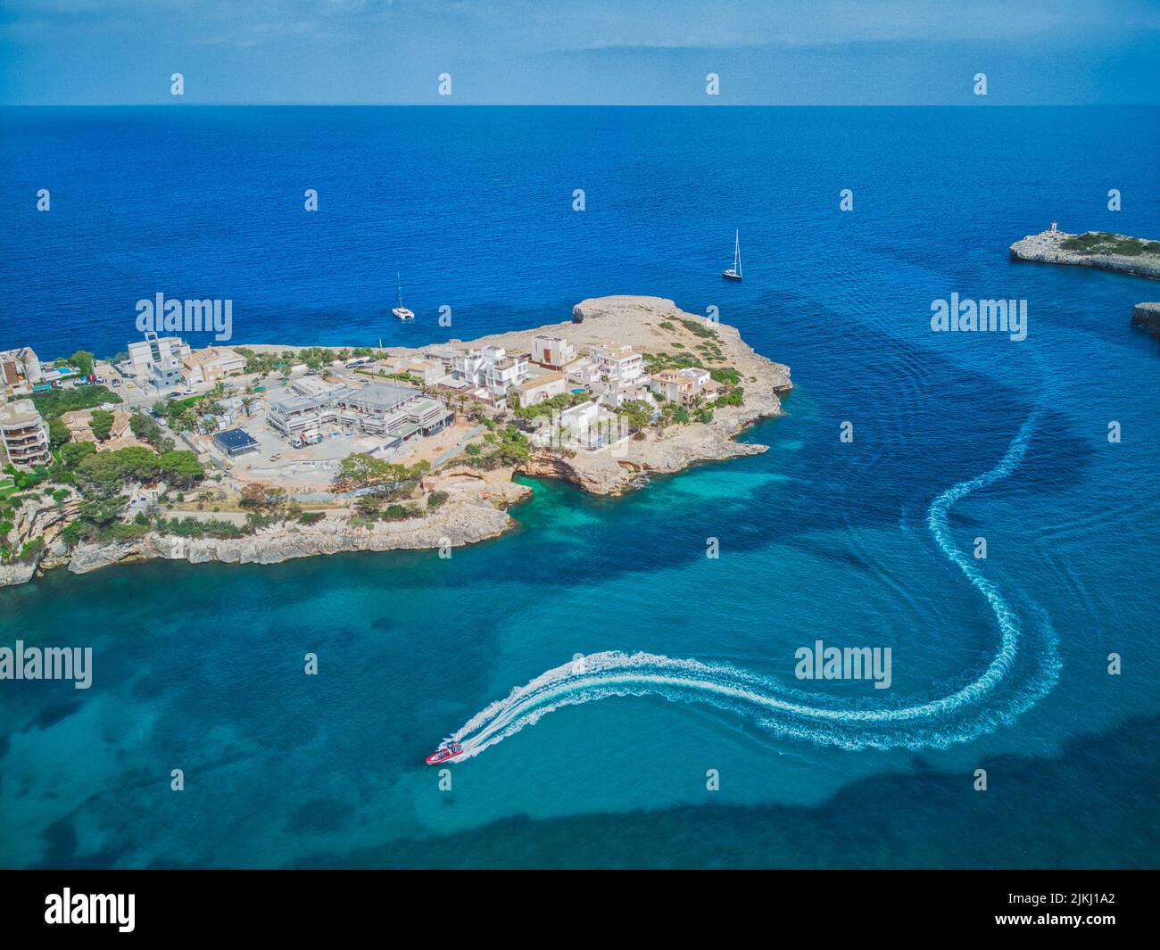 Spanien, Balearen, Mallorca, Bezirk Manacor, Portocristo. Ein Motorboot fährt in den Hafen und hinterlässt einen Pfad auf dem Meer Stockfoto