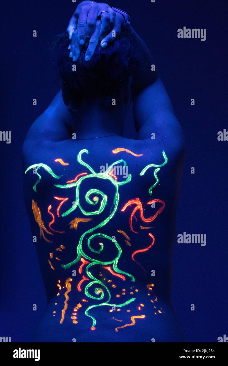 Eine vertikale Aufnahme eines weiblichen Rückens mit farbenfrohen ethnischen Fluoreszenzmustern in Neonlicht Stockfoto