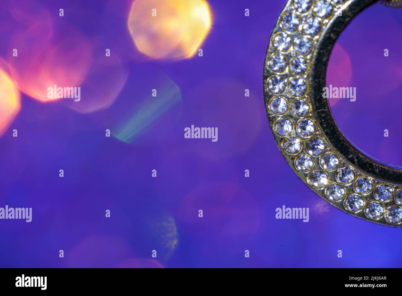 Ein Detail eines Ohrrings mit Diamanten auf violettem Blendhintergrund Stockfoto