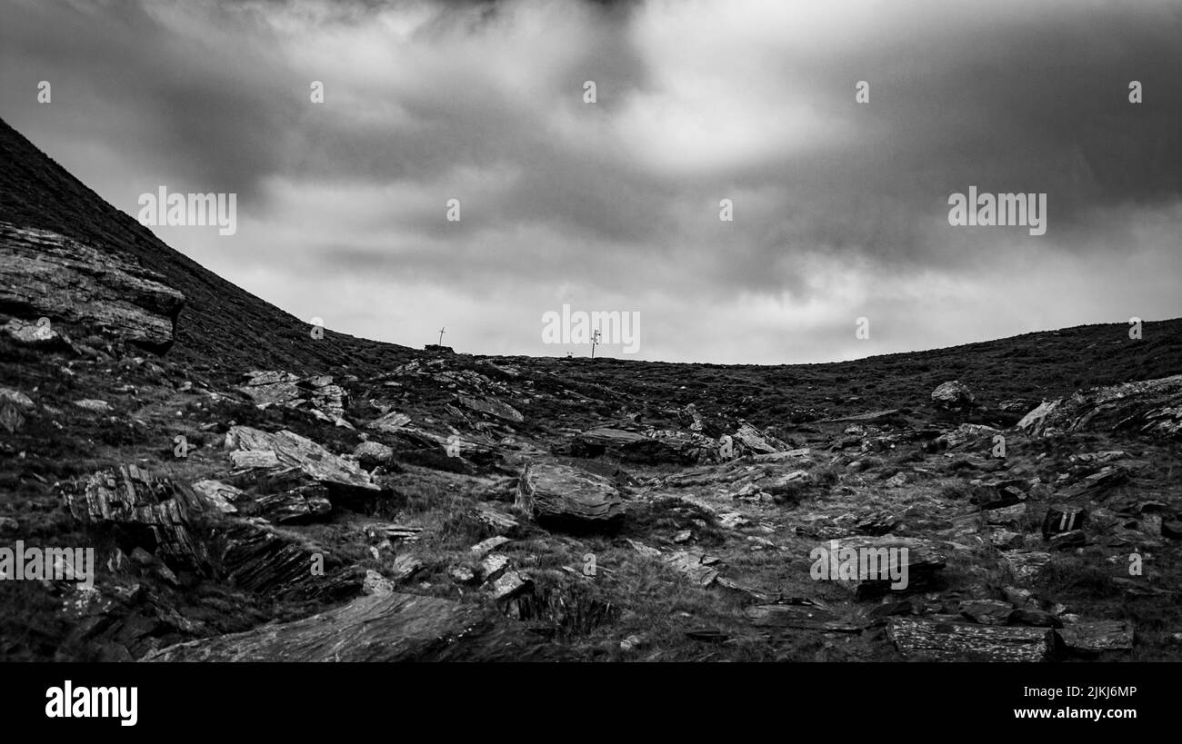 Eine Graustufenunterseite eines Wegweihens, der auf dem felsigen Hügel im Hintergrund des wolkigen Himmels festgeklebt ist. Stockfoto