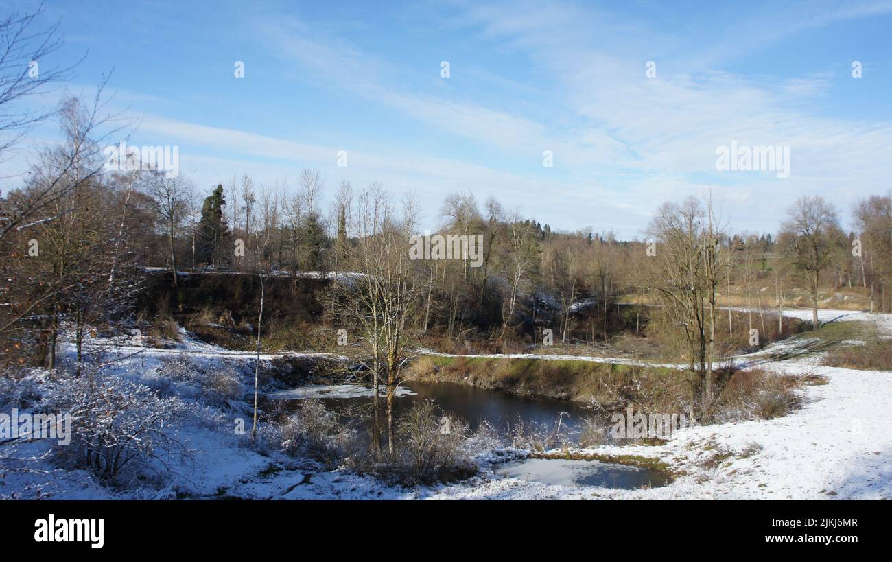Eine schöne Aufnahme eines Teiches neben einem schneebedeckten Feld im Hintergrund von blattlosen Bäumen. Stockfoto