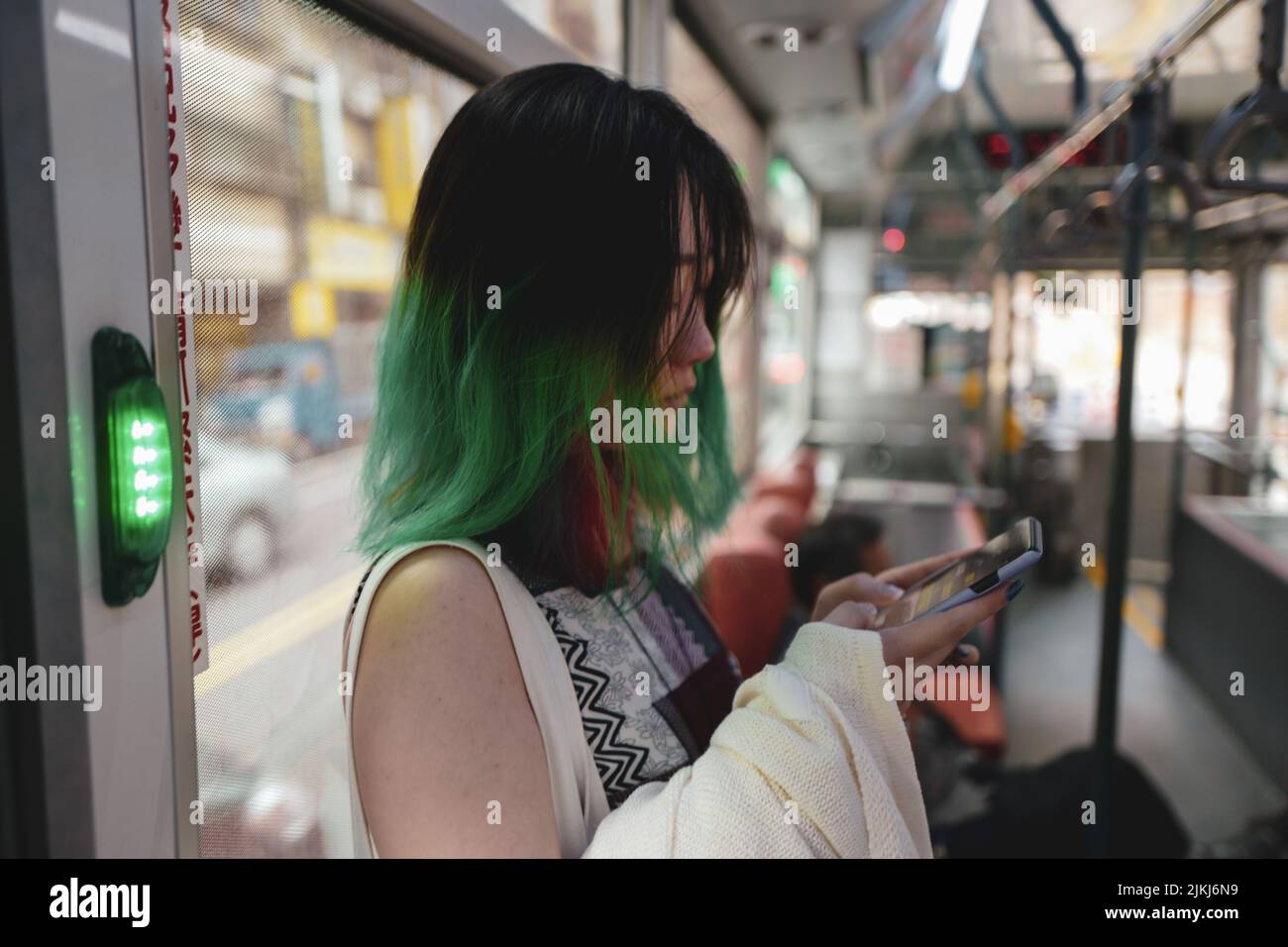 Ein asiatisches Mädchen mit grün gefärbten Haaren scrollt im öffentlichen Autobus über ihr Telefon. Stockfoto