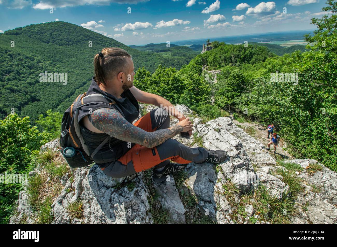 Eine Aufnahme eines jungen Wanderers mit Tattoos, die an einem sonnigen Tag auf einem Berg ruhen Stockfoto
