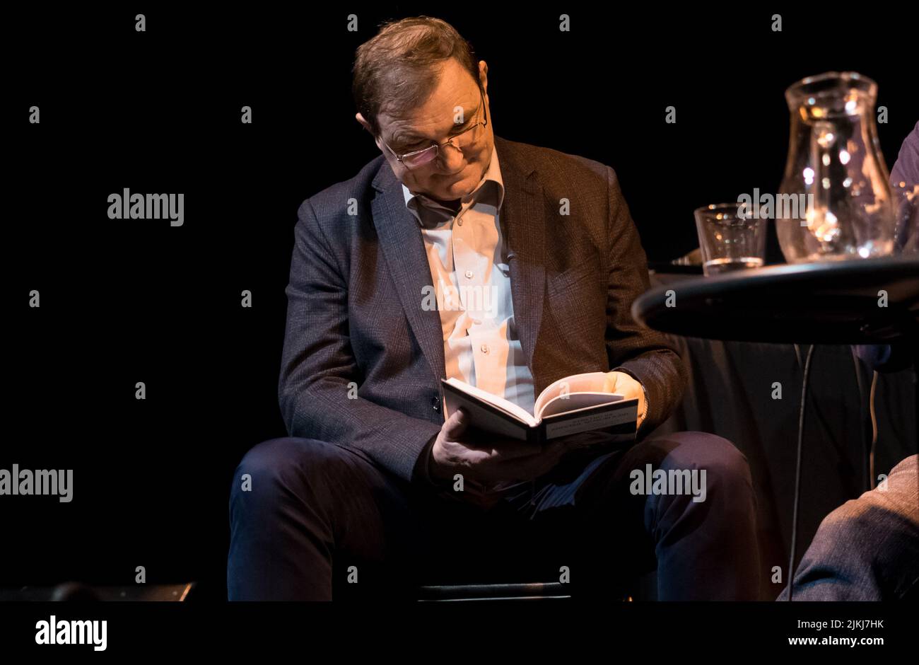 Alter Mann, der während einer öffentlichen Diskussion in Innenräumen ein Buch liest Stockfoto