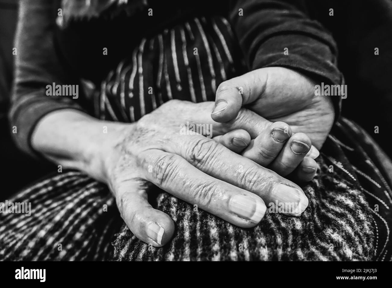 Ein junger Mann hält die faltige Hand einer älteren Frau in Schwarz-Weiß-Tönen Stockfoto