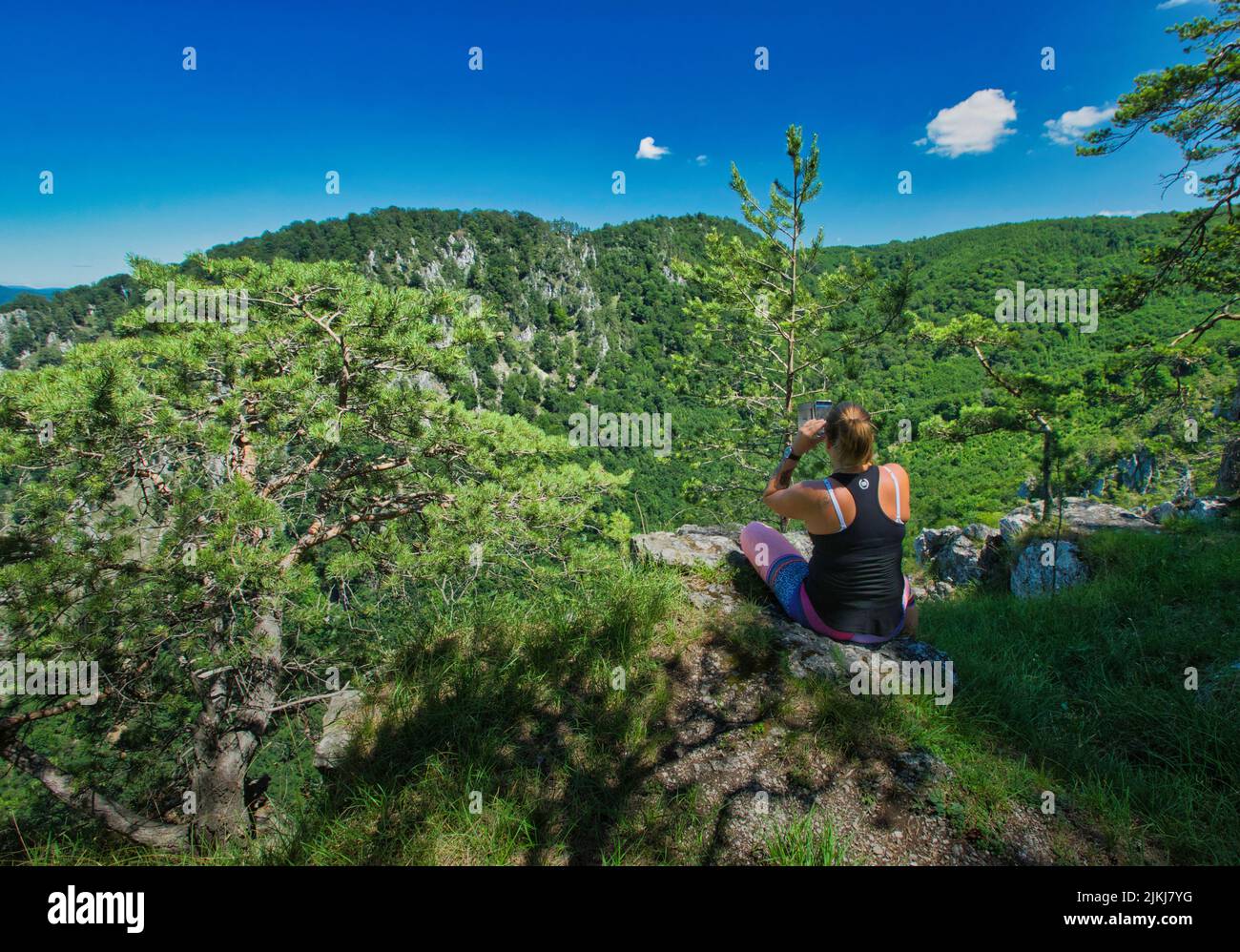 Eine Rückansicht einer Wanderin, die sich auf dem Felsen ausruht und auf der Spitze des Berges in Ruhe schaut. Stockfoto