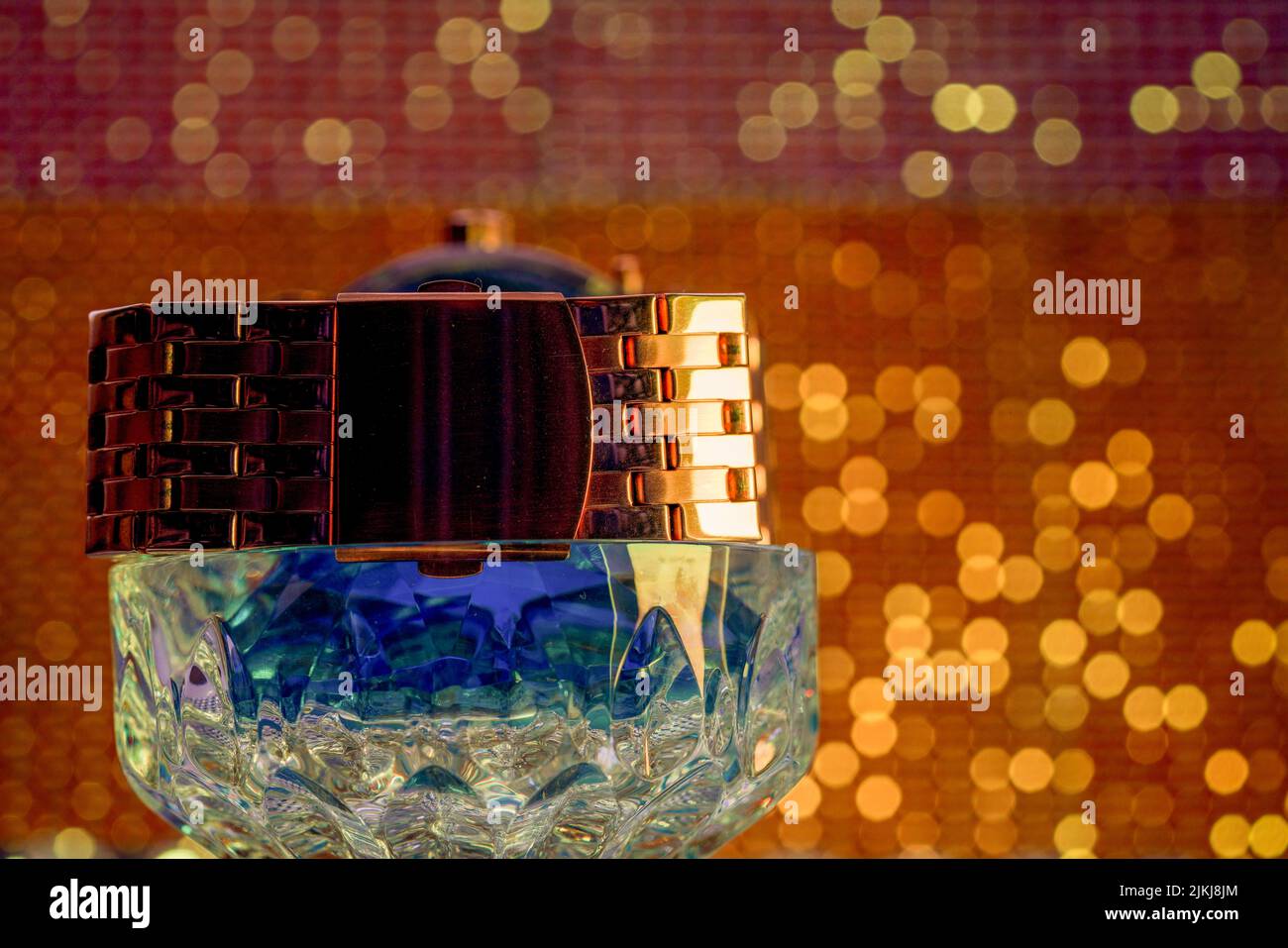 Eine goldene Armbanduhr auf einer Kristallbox vor einem blendenden Hintergrund Stockfoto
