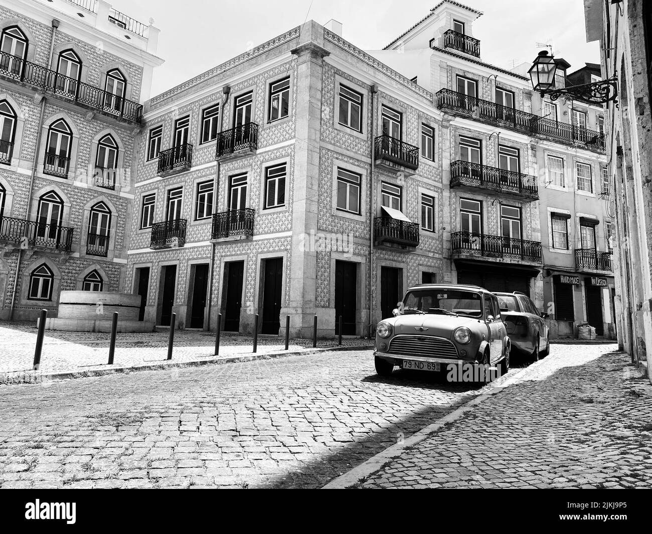 Eine Graustufenaufnahme eines Autos, das auf einer Kopfsteinpflasterstraße in Alfama, Lissabon, geparkt wurde Stockfoto