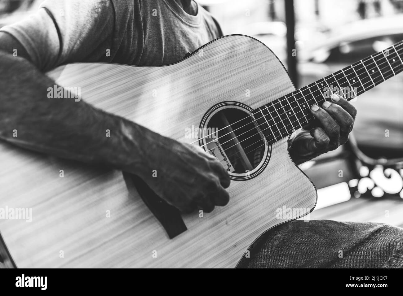 Eine Nahaufnahme eines Mannes, der im Freien Akustikgitarre spielt, in Graustufen gedreht Stockfoto