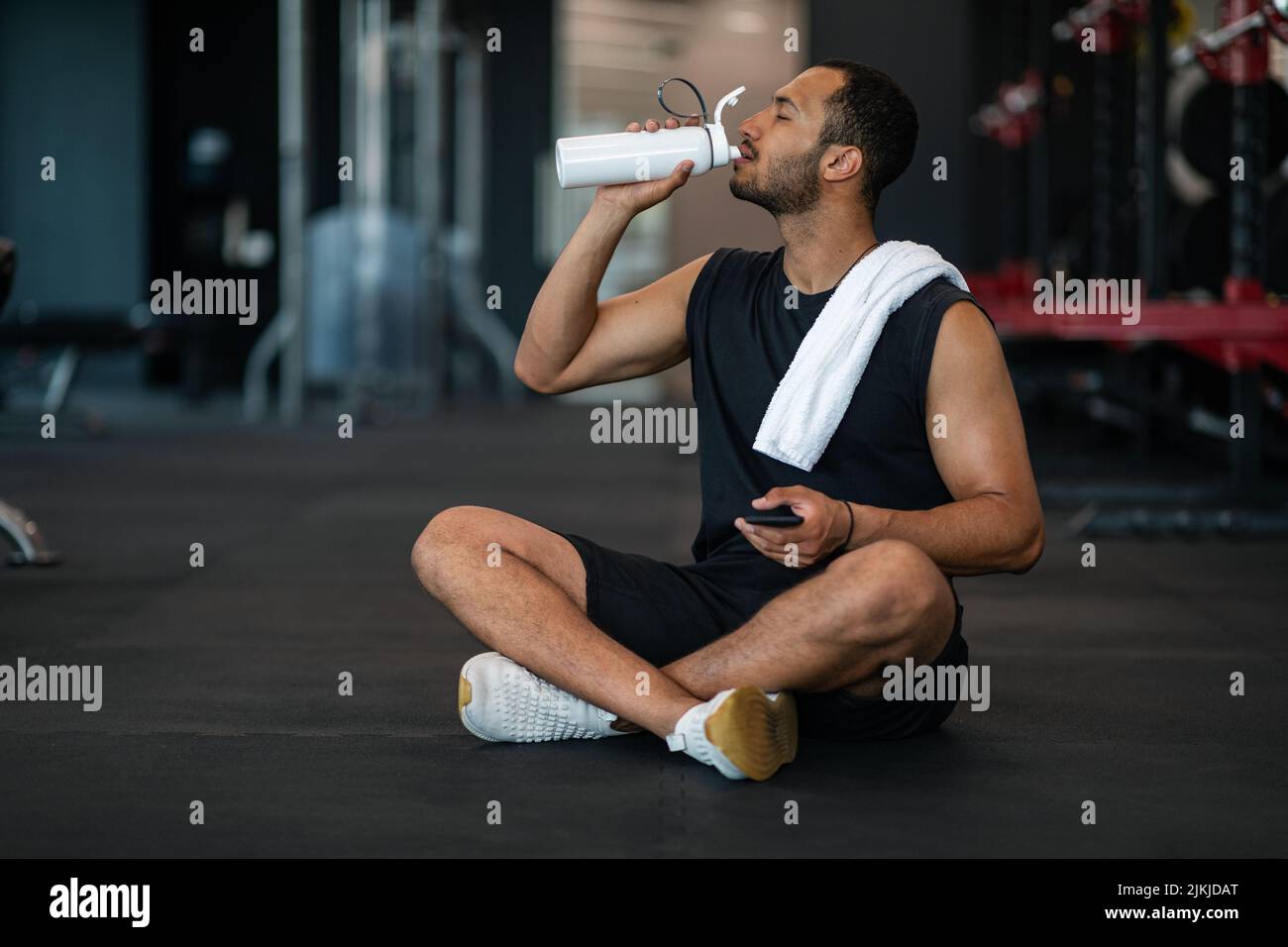 Junge Schwarze Männliche Athlet Trinkwasser Während Der Entspannung Nach Dem Training In Der Turnhalle Stockfoto