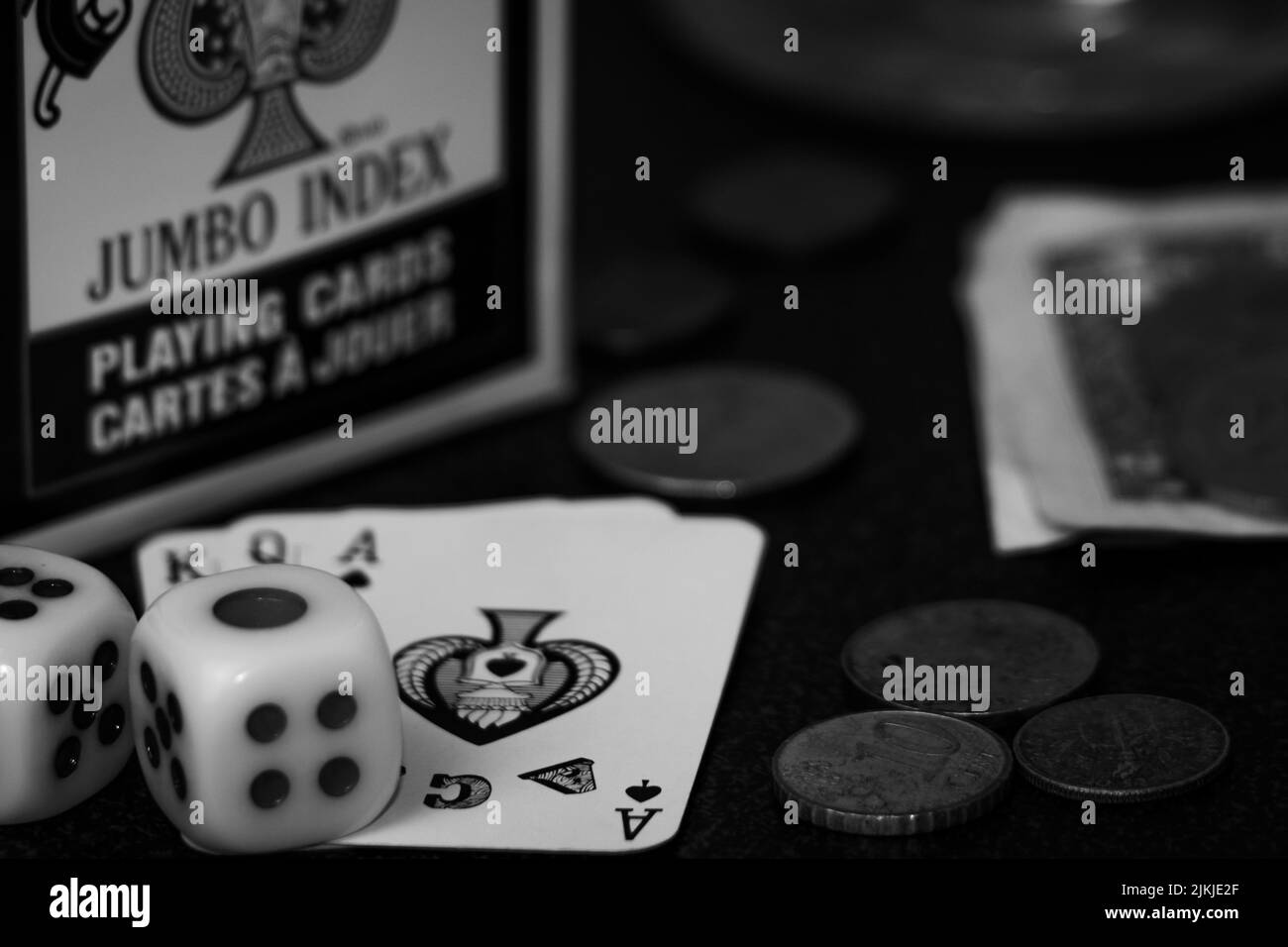 Eine Graustufenaufnahme von Spielkarten, Würfeln und Münzen auf dem Tisch - Spielkonzept Stockfoto