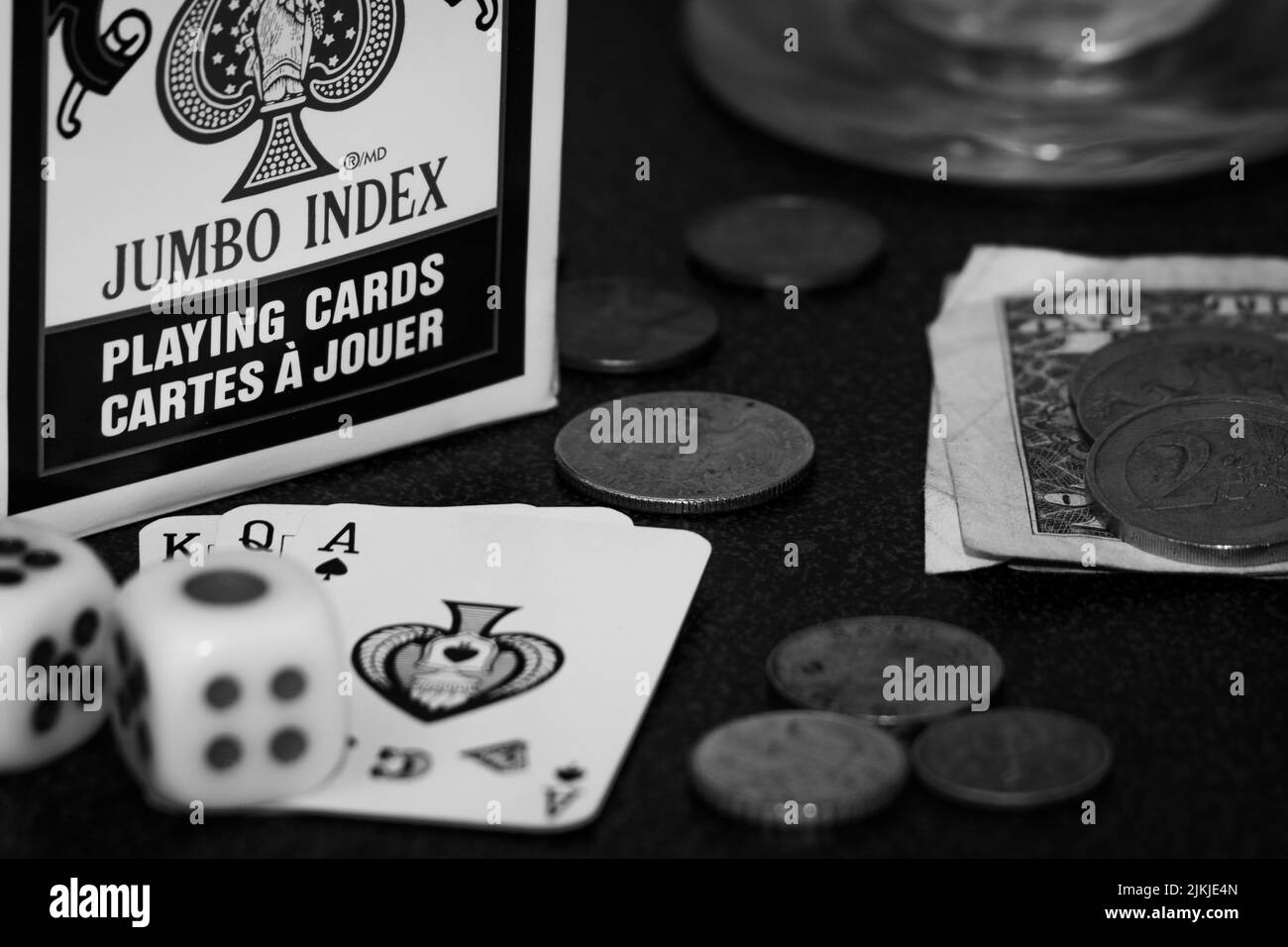 Eine Graustufenaufnahme von Spielkarten, Würfeln und Münzen auf dem Tisch - Spielkonzept Stockfoto