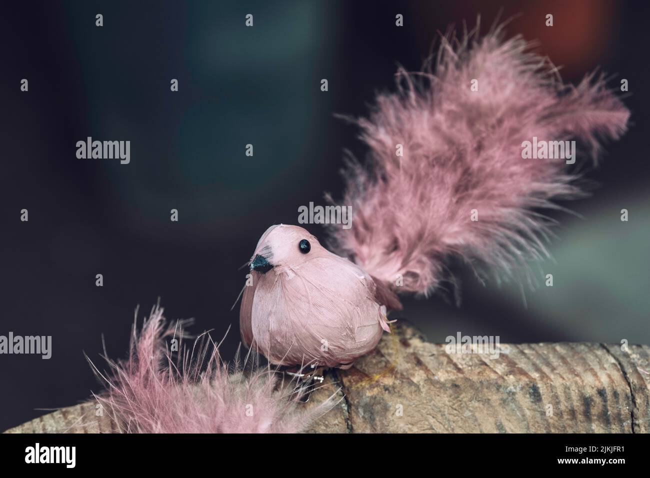 Ein flacher Fokus einer rosa Vogelfigur aus Federn auf einem Baumstamm, eine Osterdekoration Stockfoto