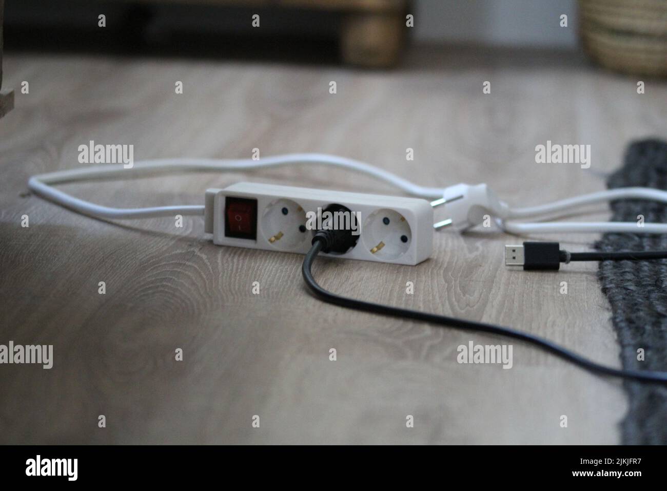 Ein weißes Verlängerungskabel auf dem Boden des Zimmers, das mit anderen schwarzen Kabeln verbunden ist Stockfoto
