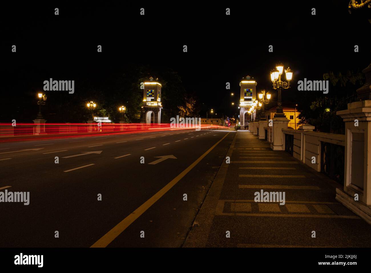 Die leichten Spuren von Autos auf einer Brücke mit Lichtmasten in der Nacht Stockfoto
