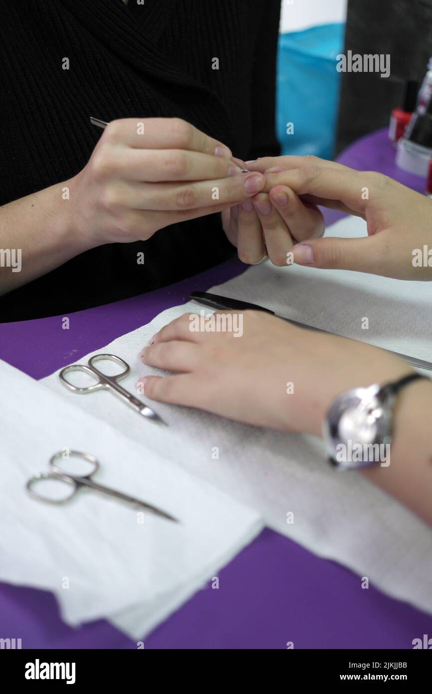 Der professionelle Manikurist tut einen Service für das Lackieren von Nägeln. Die Nagellack-Gel-Beschichtung ist so nah wie möglich an der Nagelhaut. Stockfoto