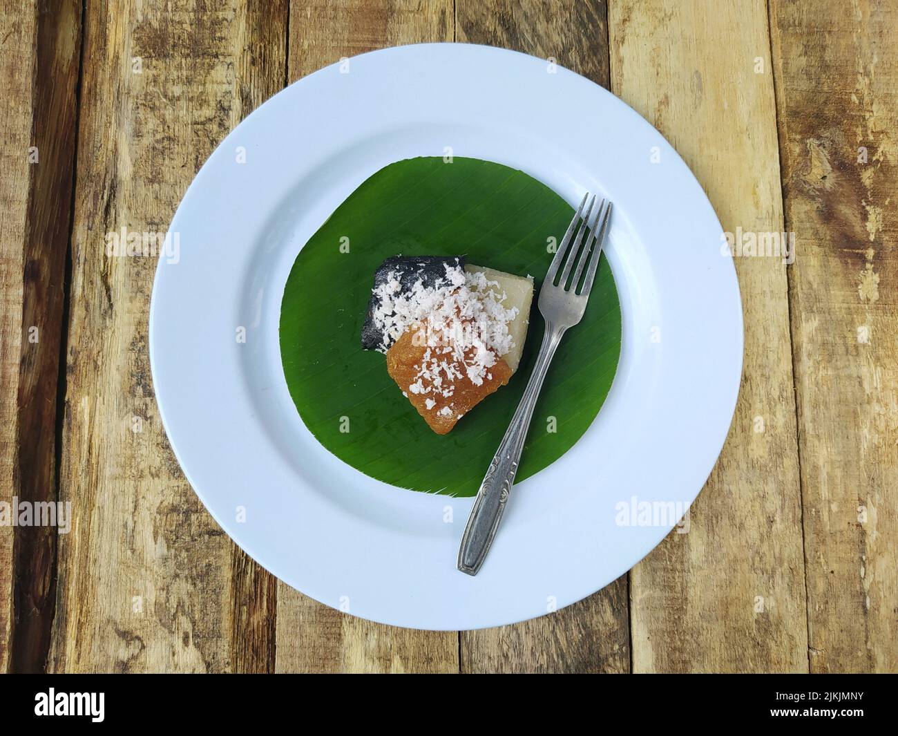 Draufsicht Getuk oder Speisen aus Maniok und Kokosnuss auf einem Teller und Bananenblatt mit Holztisch, traditionelles Essen aus indonesischem Java Stockfoto