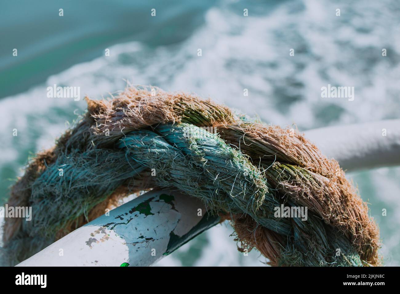 Eine Nahaufnahme eines dicken Seils, das auf einem Metallrohr auf dem Boot gelehnt ist. Stockfoto