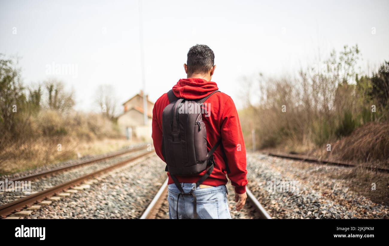 Eine Aufnahme eines Mannes von seinem Rücken mit rotem Kapuzenpullover und  Rucksack, der auf einer Eisenbahn steht Stockfotografie - Alamy