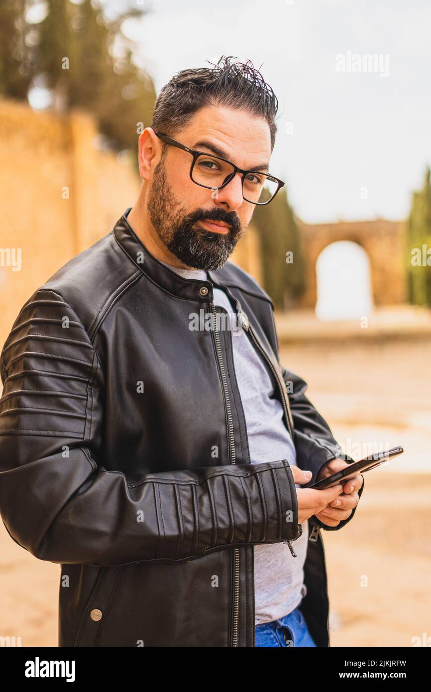 Eine vertikale Aufnahme eines jungen bärtigen Mannes in einer Lederjacke, der sein Telefon benutzte Stockfoto