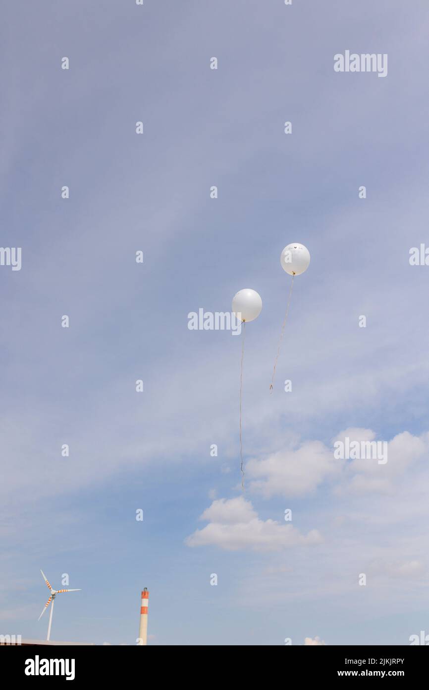 Eine vertikale Aufnahme von zwei weißen runden Ballons, die in der Luft gegen einen blauen Himmel schweben Stockfoto