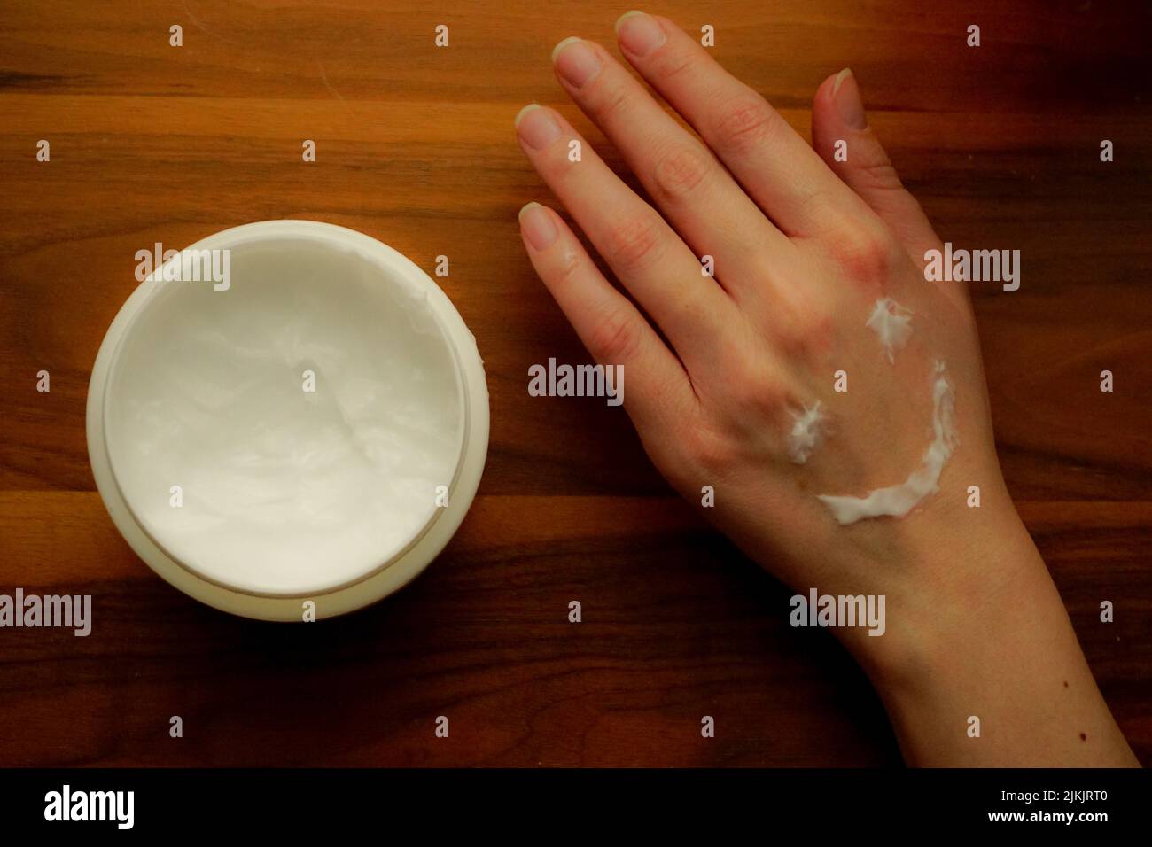 Frau trägt Handcreme auf ihre Hand auf isoliertem Holzhintergrund auf Stockfoto