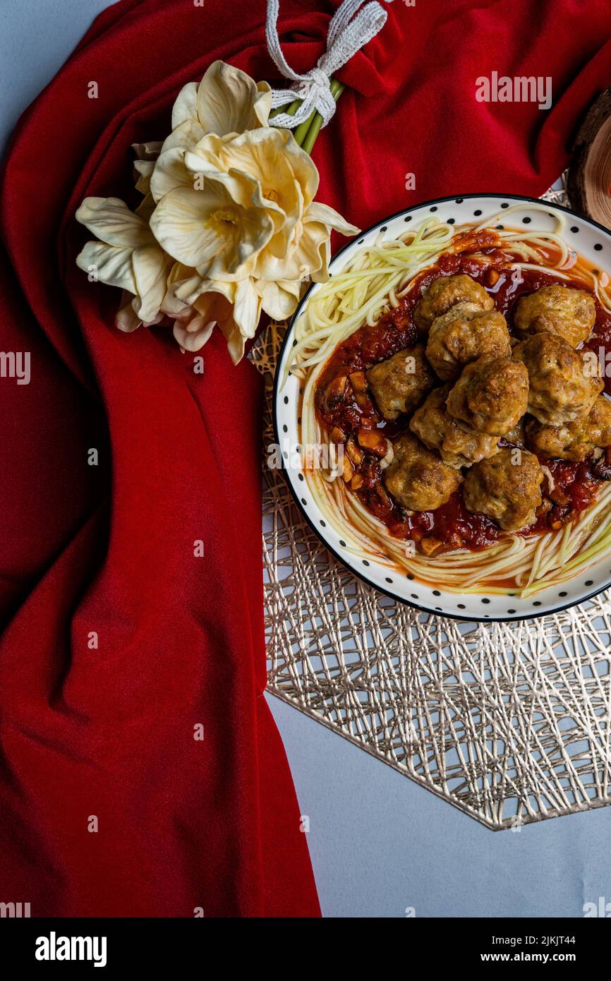 Eine Ansicht von oben von Fleischbällchen mit roter Sauce und Zucchini-Nudeln auf gefaltetem Papier und Blumenschmuck Stockfoto