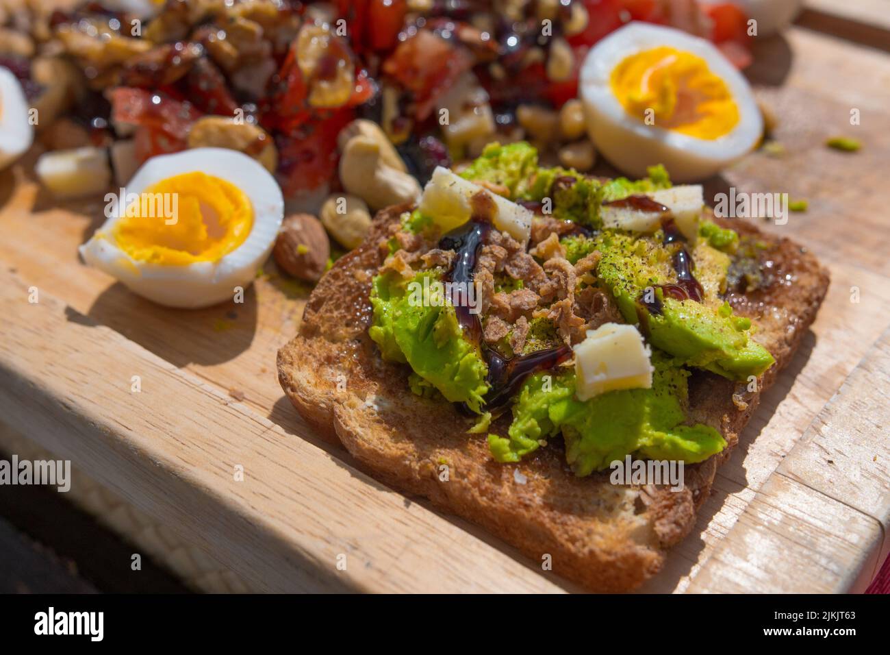 Eine selektive Aufnahme eines Toasts mit Avocado, Käse, Eiern und Geschmackstoffen auf einem Holzbrett Stockfoto