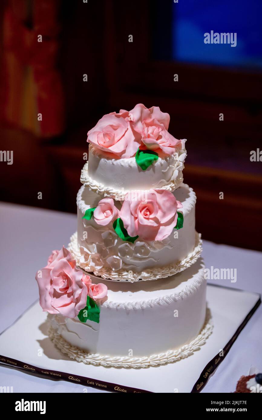 Eine vertikale Nahaufnahme der traditionellen, dreistöckigen weißen Hochzeitstorte mit rosa Rosen Stockfoto