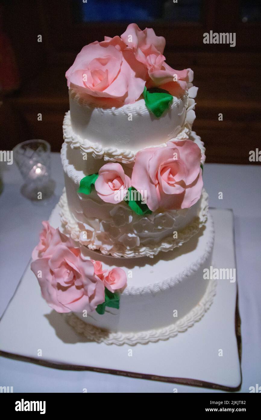 Eine vertikale Nahaufnahme der traditionellen, dreistöckigen weißen Hochzeitstorte mit rosa Rosen Stockfoto