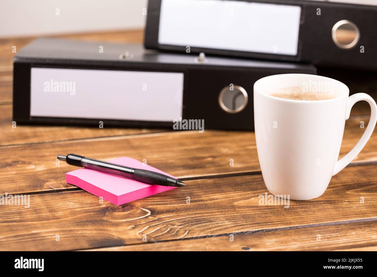 Ein Schreibtisch mit Ordnern, Haftnotizen, Stift und einer Tasse Kaffee Stockfoto