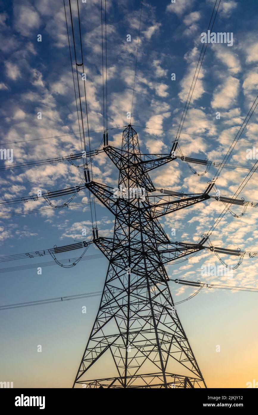 Drei Ebenen Barrel Strom Pylon Gittermast Struktur mit obenliegenden Stromleitungen bei Sonnenuntergang in Südengland, Großbritannien Stockfoto