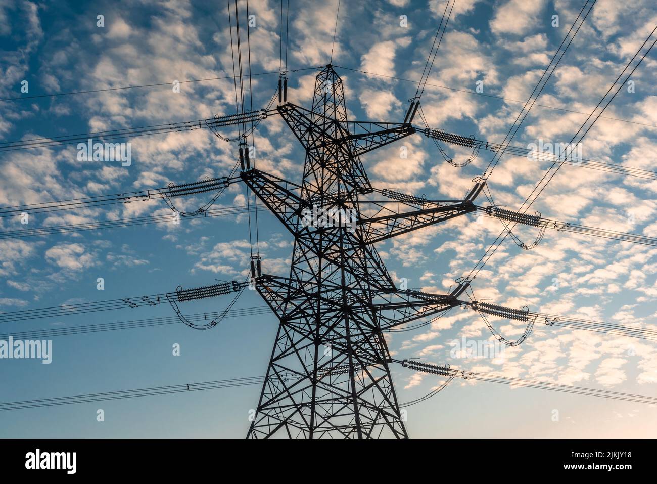 Drei Ebenen Barrel Strom Pylon Gittermast Struktur mit obenliegenden Stromleitungen bei Sonnenuntergang in Südengland, Großbritannien Stockfoto