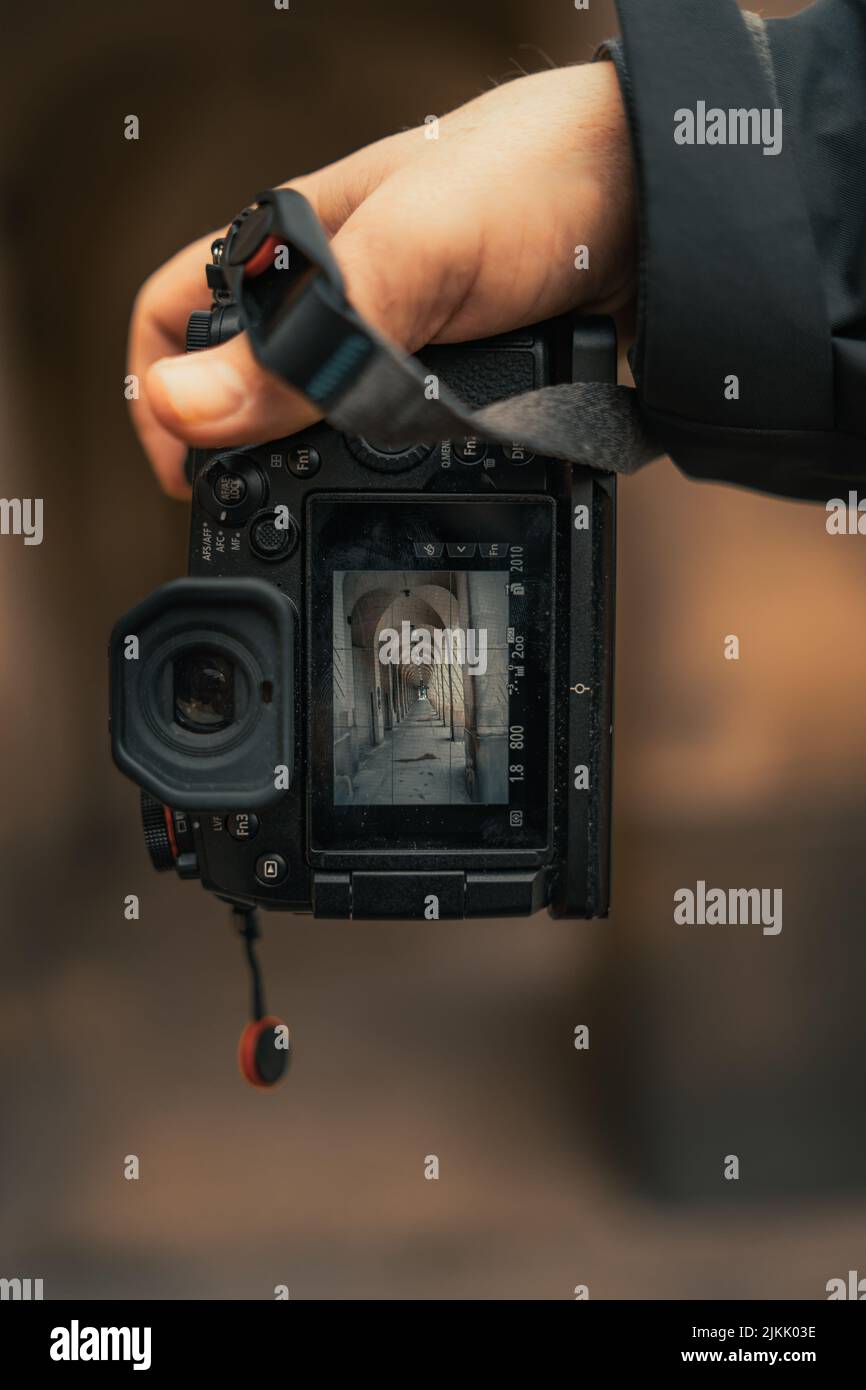 Eine Aufnahme mit einem flachen Fokus auf die Hand eines Mannes, der eine Digitalkamera hält, mit dem Foto einer historischen Arkade Stockfoto