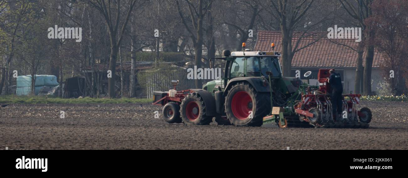 Ein Fendt-Traktor, der auf einem Feld pflügt, während ein Mann Wartungsarbeiten in Nederweert, Niederlande, anstellt Stockfoto