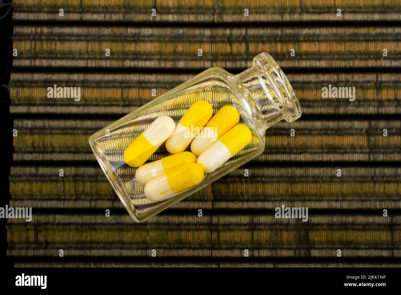 Eine Draufsicht auf eine transparente Flasche, gefüllt mit gelben und weißen Pillen auf einem gestreiften Stoff Stockfoto