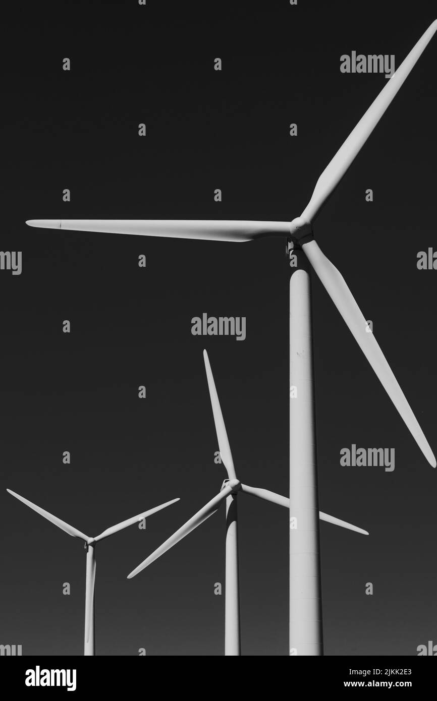 Eine vertikale Aufnahme von drei Windturbinen, isoliert auf grauem Hintergrund Stockfoto