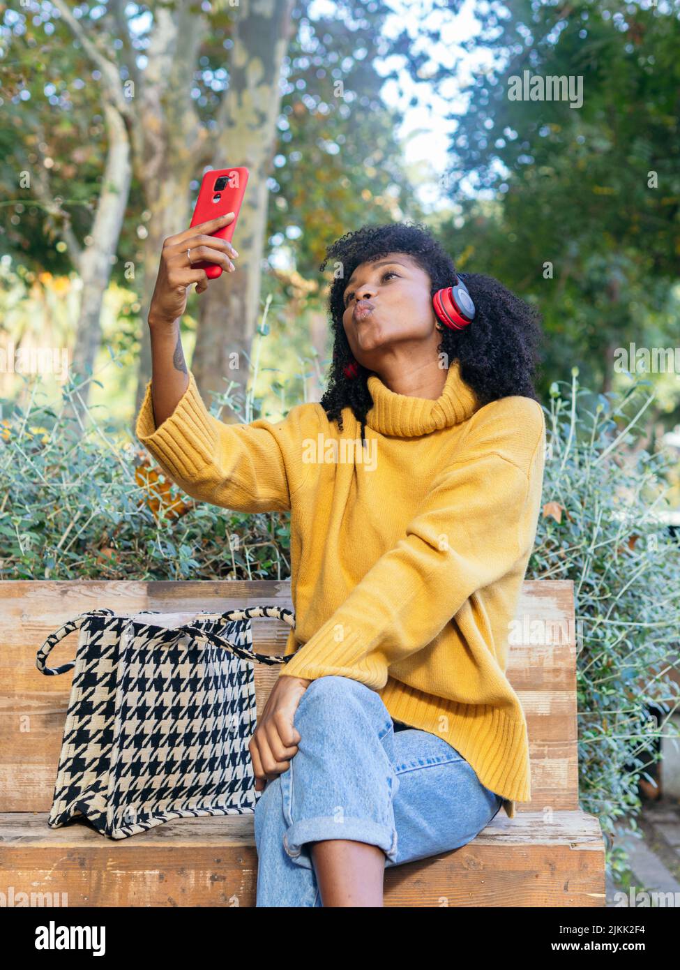 Eine Afrikanerin aus Spanien in einem gelben Pullover und Kopfhörern mit einem Telefon in der Hand Stockfoto