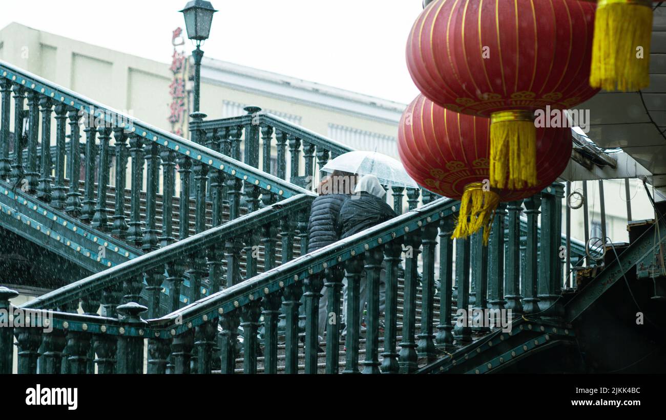 Zwei Frauen, die auf einer Treppe mit einem Regenschirm und chinesischen Laternen laufen Stockfoto