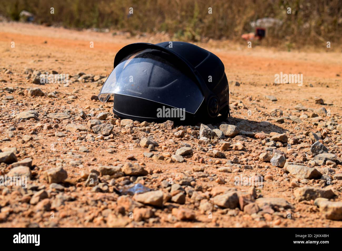 Stock Foto eines schwarzen Helm gehalten auf einer rauen Straße mit rotem Boden bedeckt. Aufnahme unter dem heißen Sonnenlicht in Bangalore, Karnataka, Indien Stockfoto