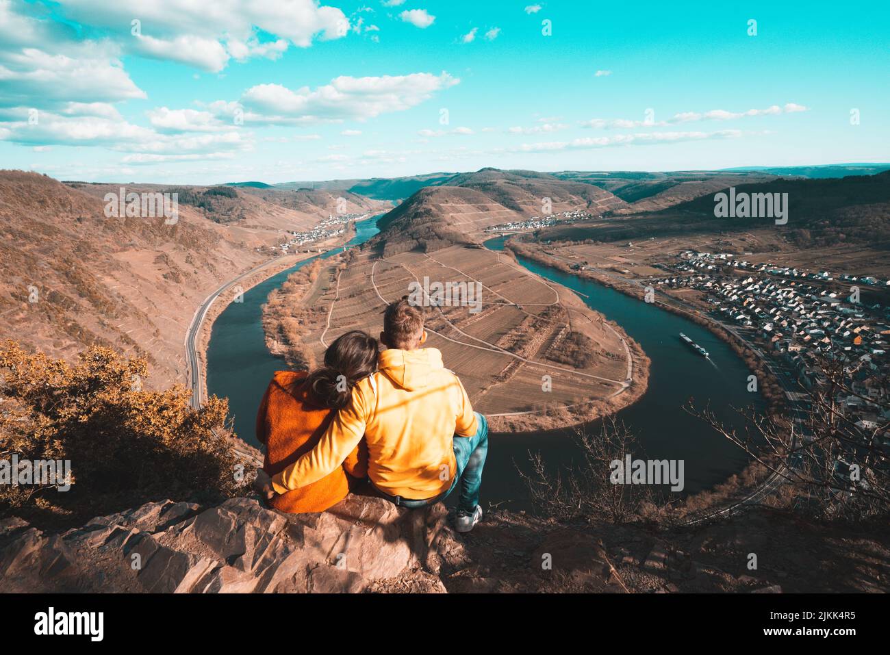 Eine Rückansicht eines Paares, das am Rand einer Klippe sitzt und auf den Fluss blickt Stockfoto
