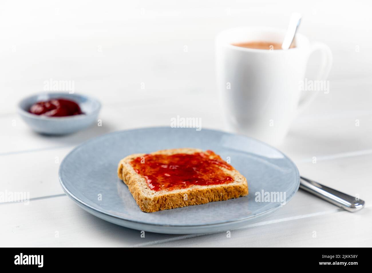 Toast mit Erdbeermarmelade auf einem blauen Teller und Tasse Von Kakao auf einem weißen Holzhintergrund Stockfoto