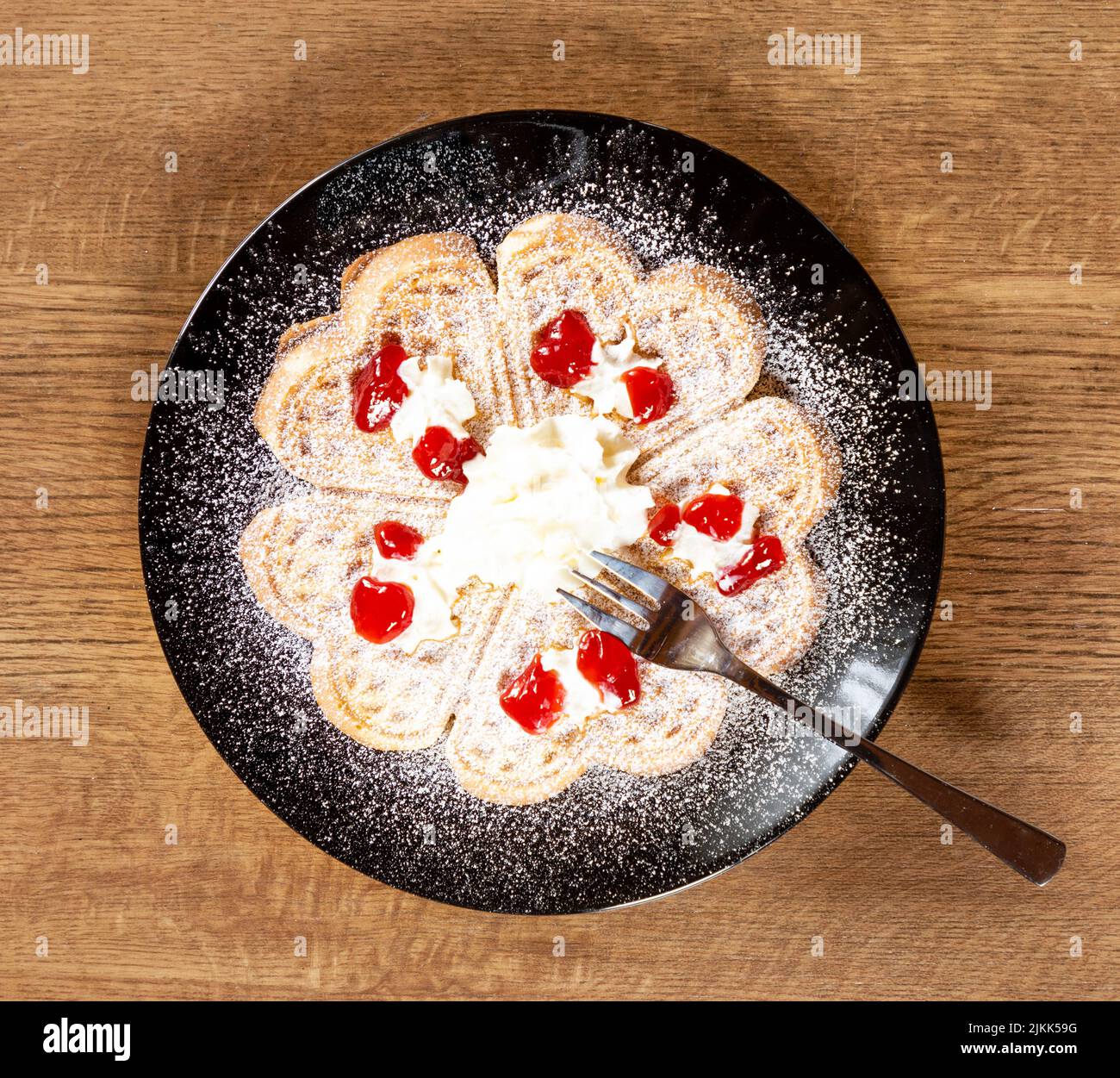 Frische Waffel auf einem schwarzen Teller mit Holzhintergrund mit Creme und Gelee Stockfoto