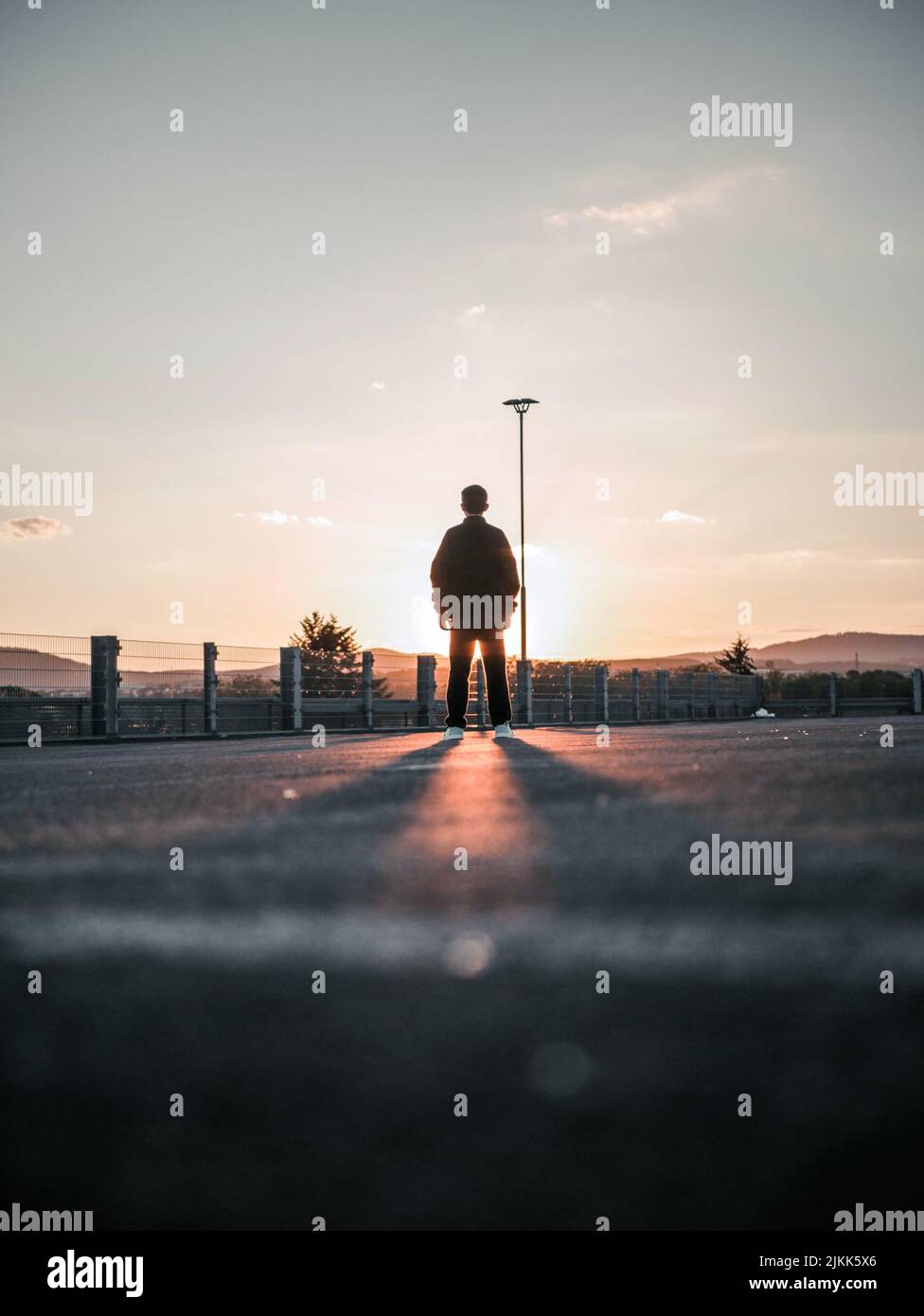 Eine vertikale Aufnahme aus dem niedrigen Winkel einer Rückansicht eines Mannes, der bei Sonnenuntergang auf der Straße steht Stockfoto