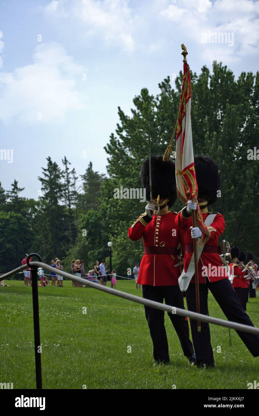 Eine vertikale Aufnahme von zwei königlichen Führern, die eine Flagge halten und auf einem grünen Gras in einem Park in Kanada stehen Stockfoto